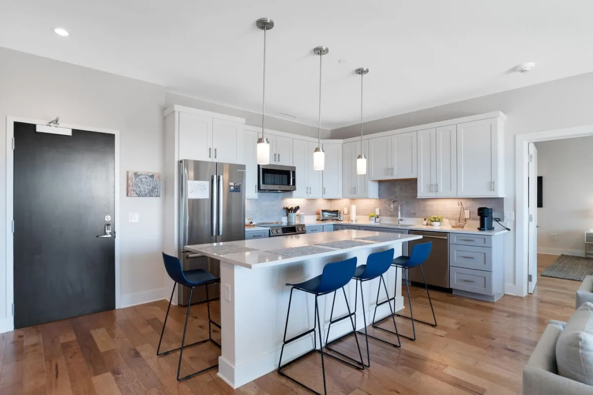 A modern, open kitchen with a sleek island countertop, bar stools for casual seating, stainless steel appliances, and contemporary cabinetry. The layout is ideal for cooking together, sharing drinks before a night out, or hosting a group meal.