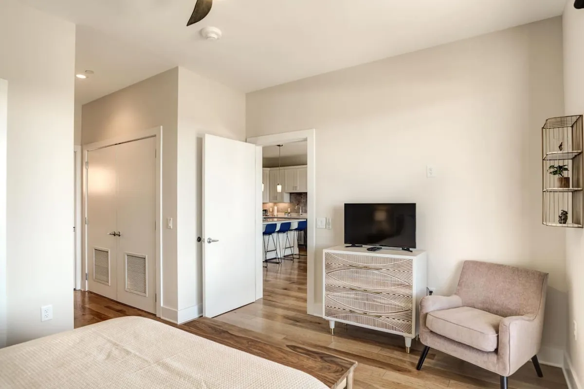 A cozy bedroom with a comfortable bed, television, armchair, and decorative shelving, creating an inviting atmosphere for relaxing or unwinding after a night out.