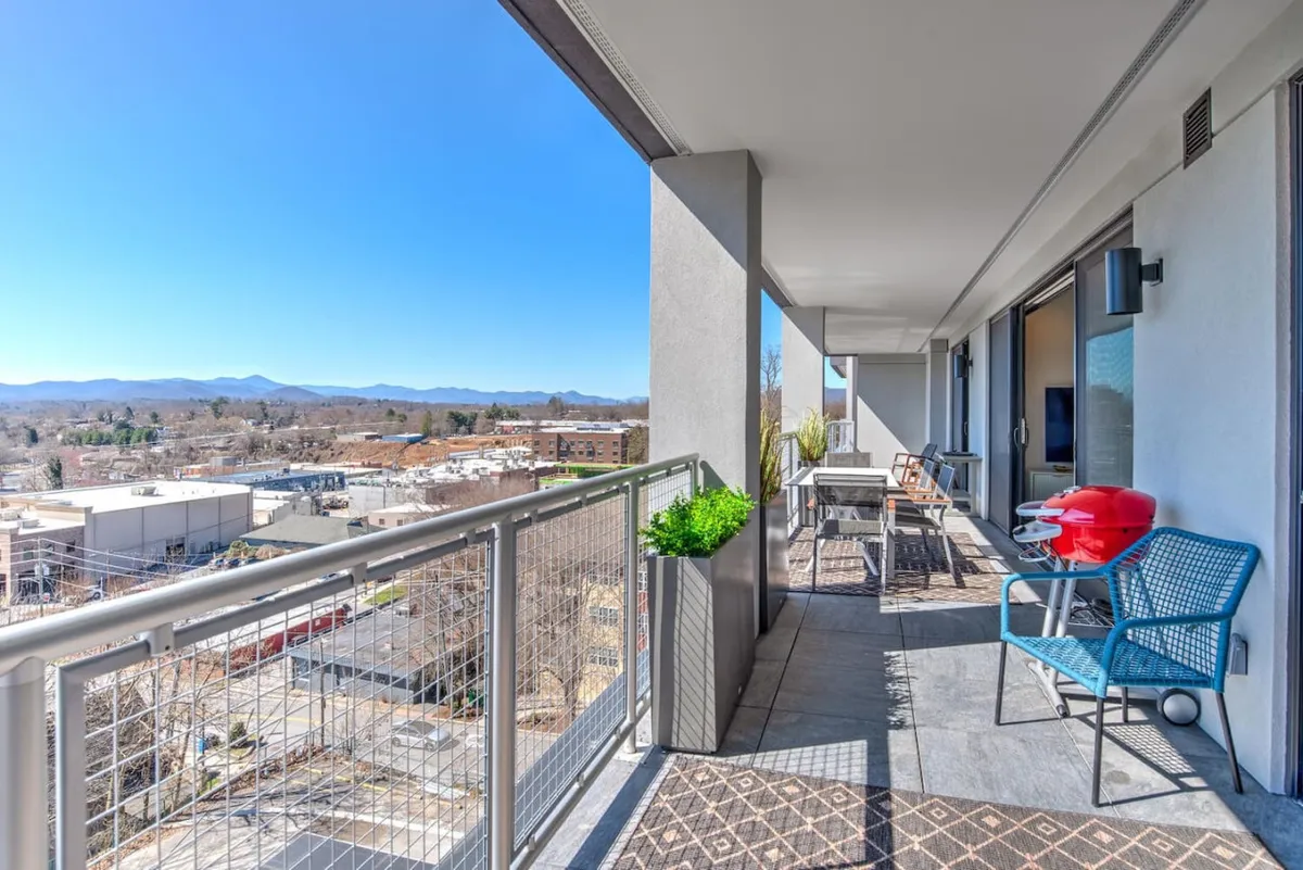 A cheerful and relaxed balcony scene featuring a railing, a grill, a cozy seating area, and planters, all framing a view of the mountains. The scene is lively, suggesting barbecuing, socializing, and soaking in the surrounding beauty.