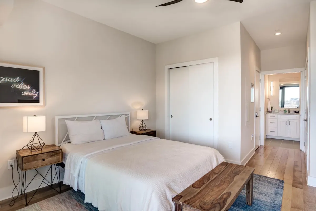 A serene bedroom featuring a plush bed with soft linens, complemented by nightstands and elegant framed art. A closet door is visible, suggesting ample storage. The overall mood is tranquil and inviting, ideal for relaxing after a scenic day out.