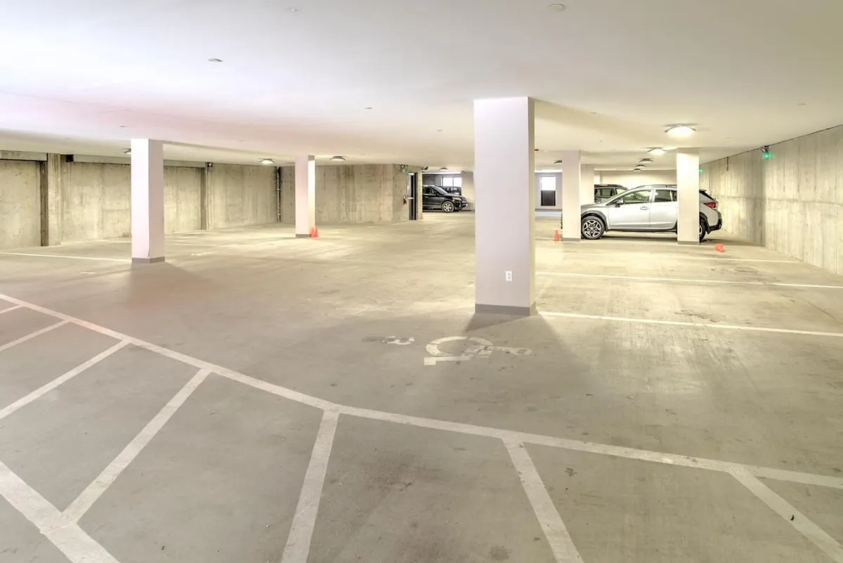 A spacious, well-lit garage interior with clearly marked parking spaces, visible concrete pillars, and several parked cars. The environment is clean and secure, suggesting easy access and peace of mind for vehicle owners.