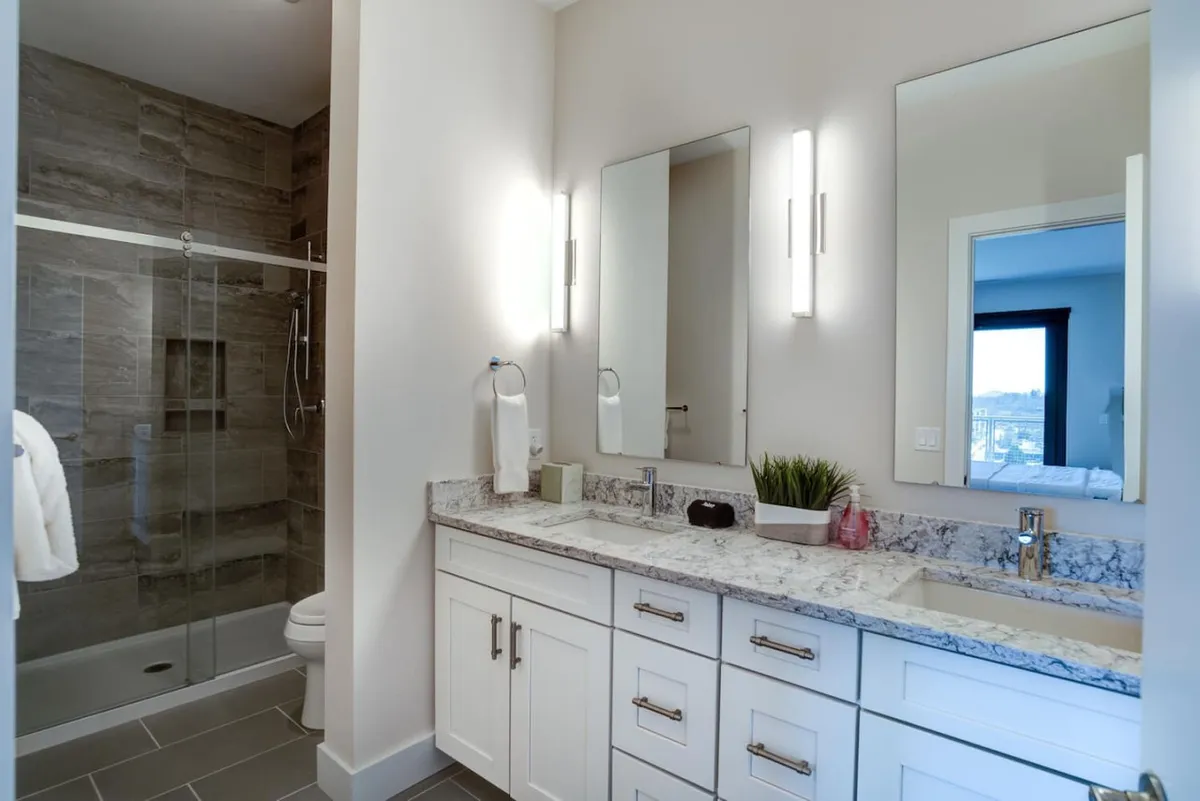 A modern vanity with dual sinks, expansive mirrors, and a glass shower enclosure. The bright space exudes a fresh, spa-like vibe, perfect for unwinding and personal moments after a day of exploring the mountains or local attractions.