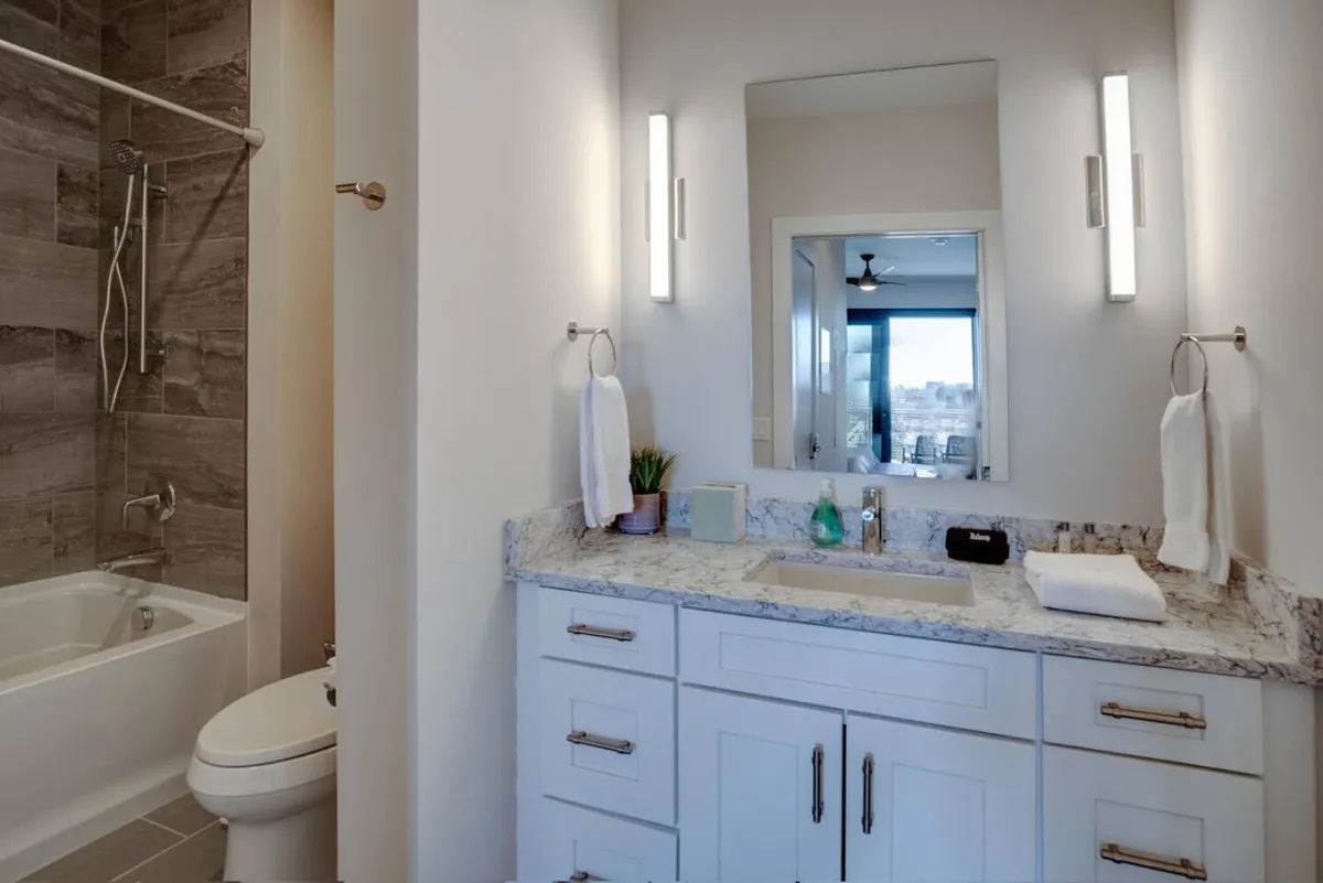 A modern bathroom with a granite countertop, large mirror, and a spacious bathtub/shower area. The space is immaculate and inviting, ideal for both refreshing morning routines and unwinding after a day of adventure.